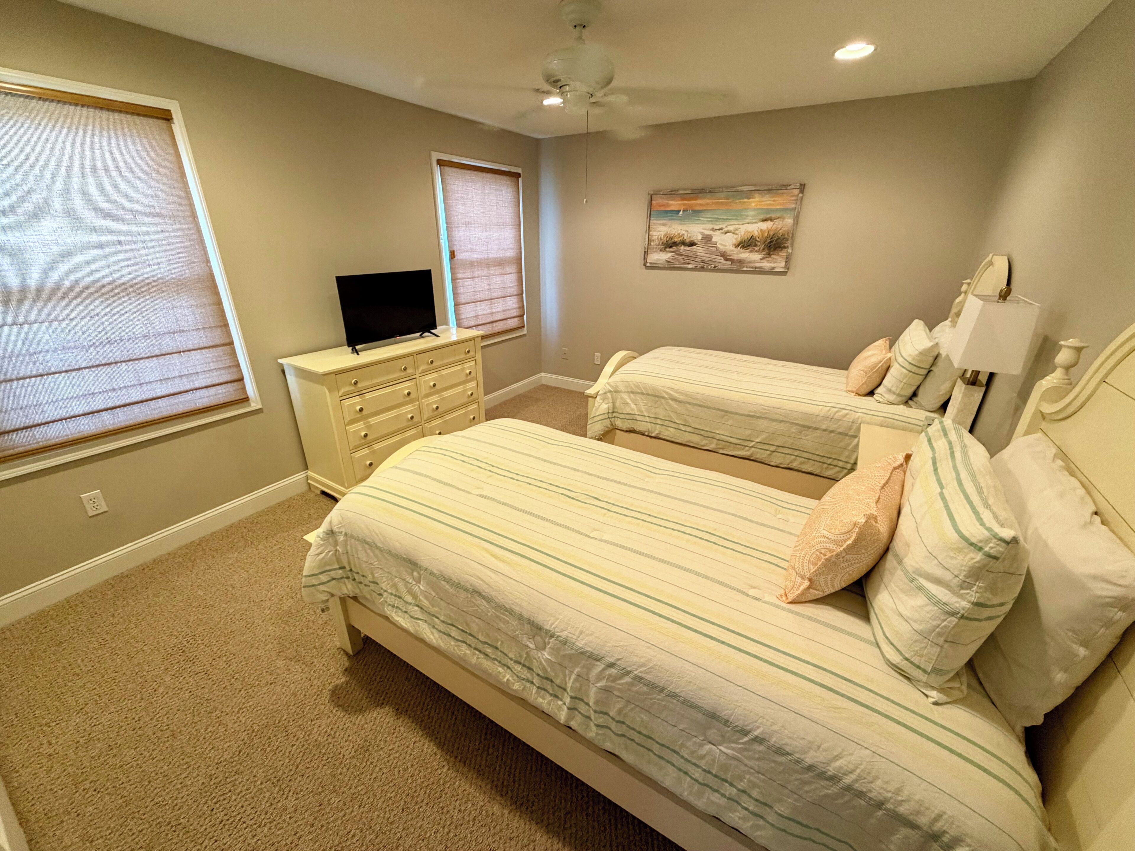 A bedroom with two beds, a dresser, a television, and a painting on the wall.