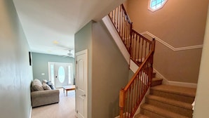 Un escalier avec des balustrades en bois, des marches recouvertes de moquette et une porte donnant sur une pièce dont un mur est peint en bleu clair et qui est équipée d’un ventilateur de plafond.