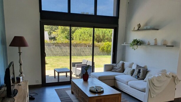 Un soggiorno moderno con un divano bianco, un tavolino in legno e un televisore su un mobiletto in legno. Una porta scorrevole in vetro dà accesso a una zona patio con mobili da esterno.