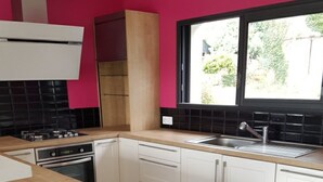 Una cucina con mobili bianchi, un piano di lavoro in legno, uno schienale piastrellato nero e una finestra che si affaccia sul verde.