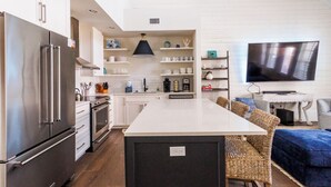 Una cocina moderna con electrodomésticos de acero inoxidable, una isla central y un comedor con mobiliario de mimbre.