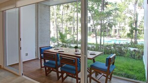 Ein Essbereich mit Tisch und Stühlen, eine Glastür zum Poolbereich und Blick auf Pool und Grünfläche.
