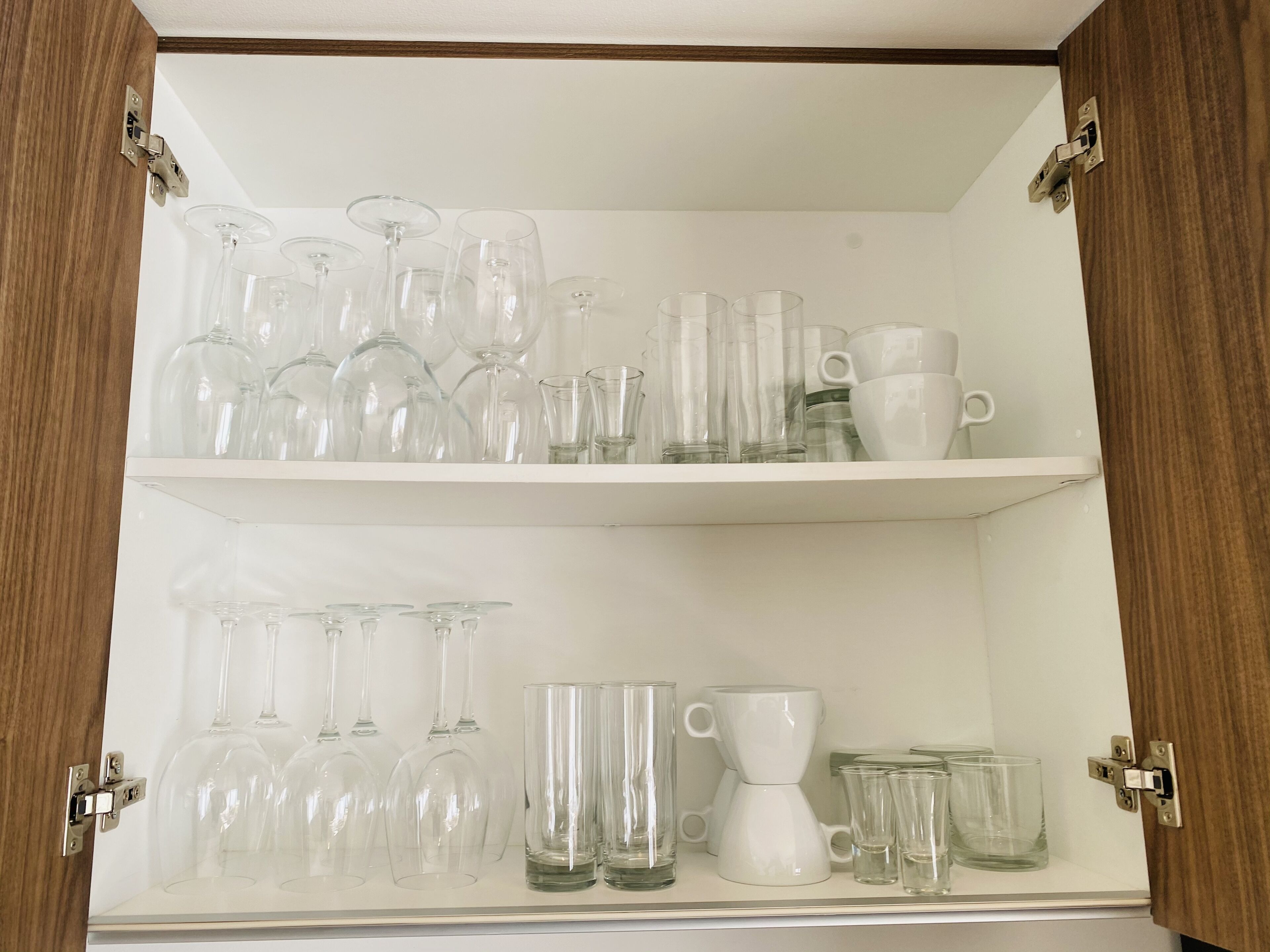 Un meuble avec deux étagères contenant divers articles en verre, notamment des verres à vin, des verres à cocktail et des tasses.