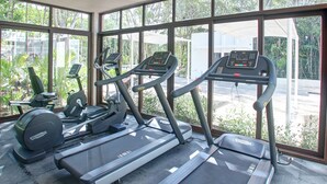 Ein Fitnessstudio mit Laufbändern, Crosstrainern und Ergometer, große Fenster mit Blick auf Grünflächen und einen Parkplatz.