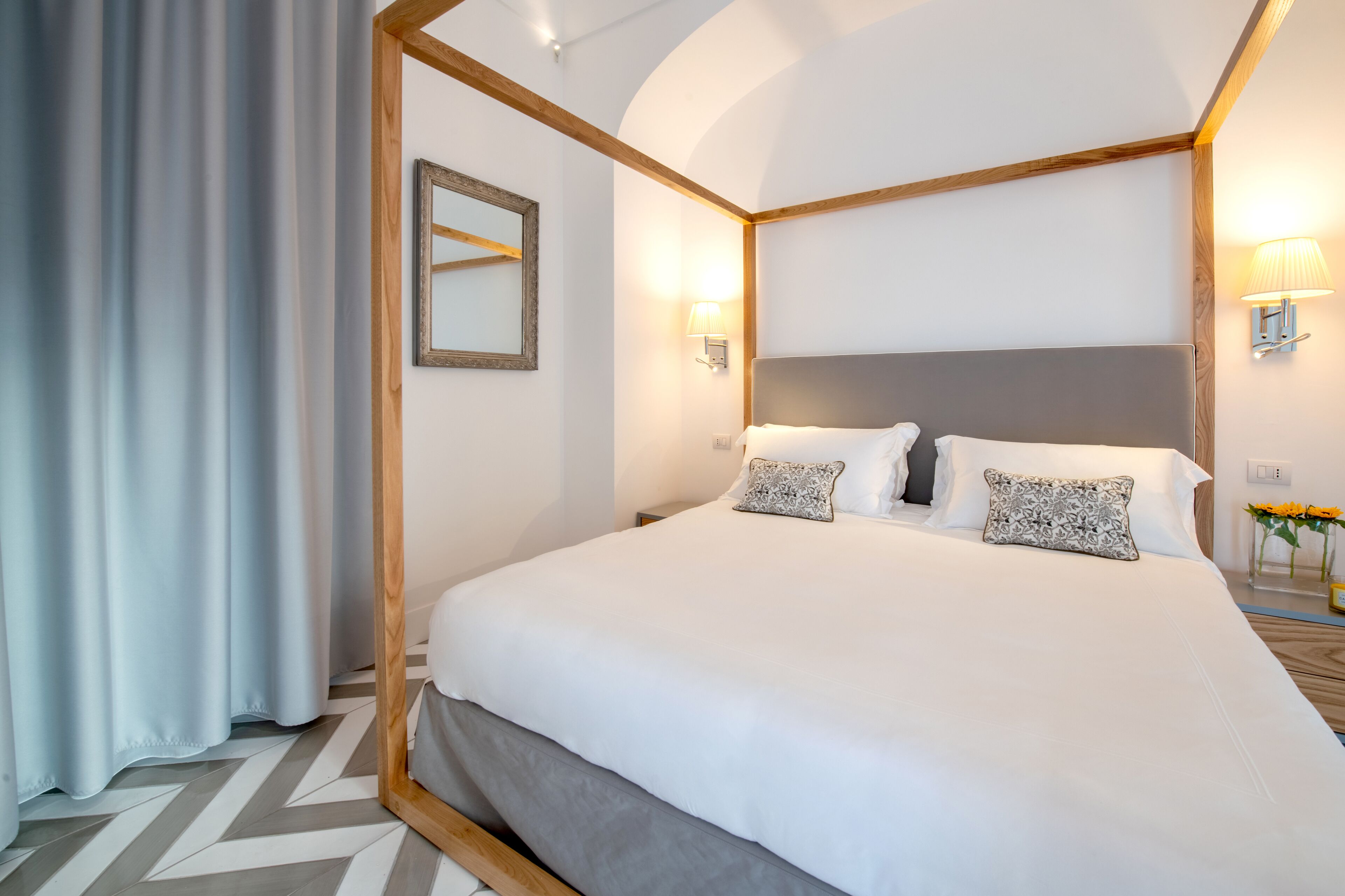 Un lit bien fait, avec du linge de lit blanc et des coussins à motifs, une tête de lit en bois et un miroir au mur.