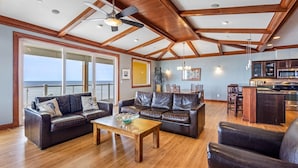 A spacious living room with leather sofas, a wooden coffee table, and a view of the ocean through large windows. - WV31 Sky Surfer by First Flight Rentals (Rodanthe)