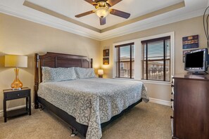 Une chambre à coucher comprenant un lit, une table de chevet, une lampe, un ventilateur de plafond, une commode et un téléviseur.