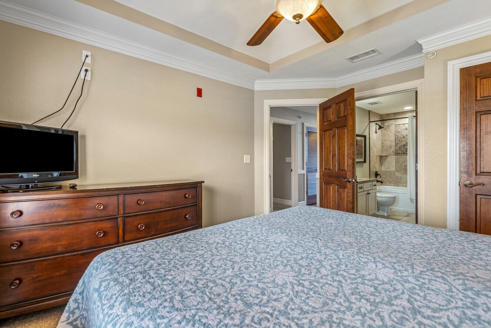 A bedroom with a bed, dresser, television, and a ceiling fan.