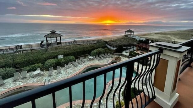Un balcon avec vue sur l’océan au coucher du soleil, un belvédère et un espace piscine.