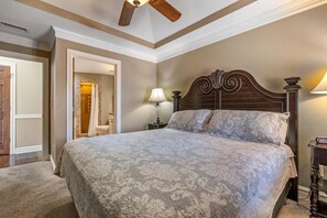 A bedroom with a large bed, a ceiling fan, a nightstand with a lamp, and a door leading to a bathroom. - CSC4I The Platinum Suite by First Flight Rentals (Kill Devil Hills)