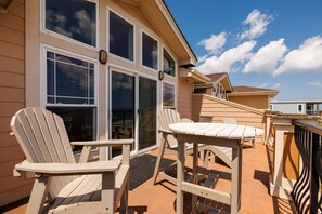 A deck with Adirondack chairs and a table, overlooking a building with large windows. - CSC4I The Platinum Suite by First Flight Rentals (Kill Devil Hills)