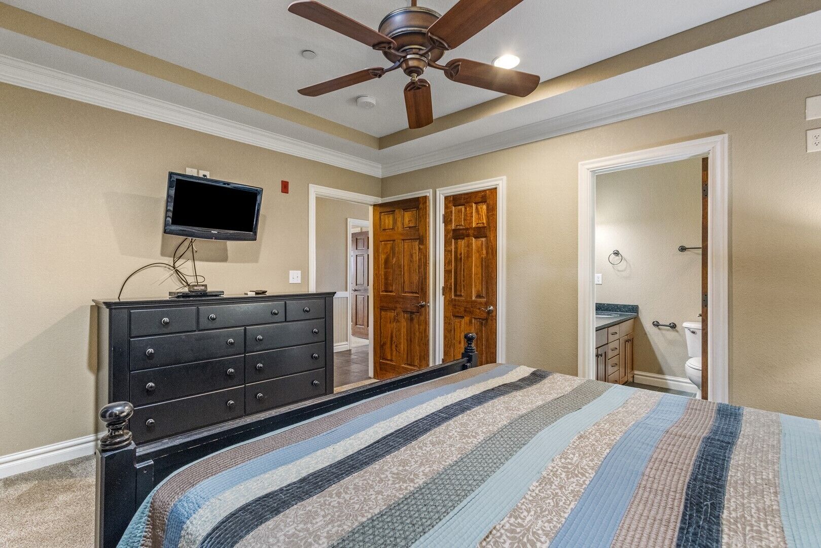 A bedroom with a bed, a dresser, a television, and a ceiling fan.