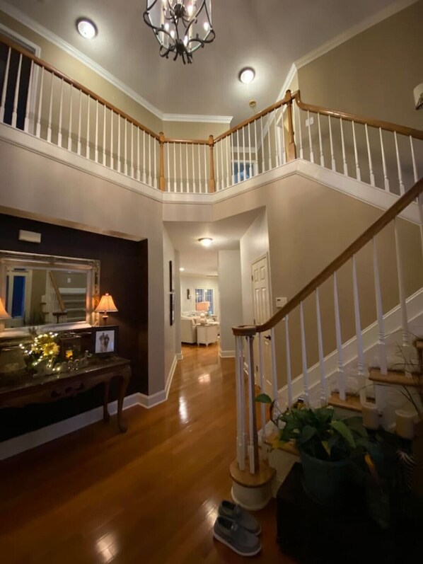 A spacious foyer with a wooden staircase, a chandelier, and a desk with a lamp.