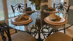 Une table à manger dressée pour quatre personnes, avec un vase de fleurs au centre, entourée de chaises dotées d’assises rembourrées.