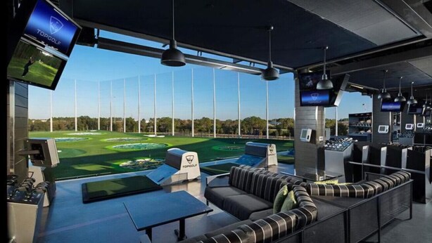 Une salle de simulation de golf moderne, dotée d’un grand écran, de sièges confortables et de plusieurs moniteurs.