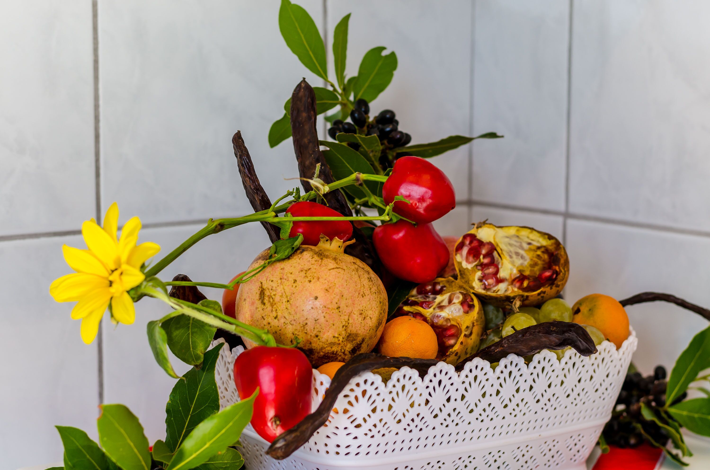 Una cesta con frutas y verduras, incluyendo tomates, granadas y una flor amarilla.