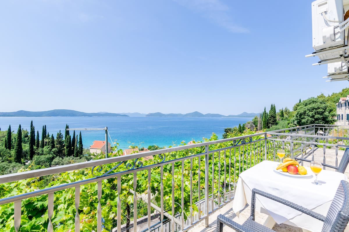 Un balcón con una mesa lista para una comida, con vistas a un paisaje costero con viñedos y el mar.