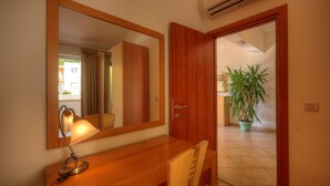 A hotel room with a wooden desk, a desk lamp, a chair, a large mirror, a wooden door, and a potted plant. - Apartment Villa Molina (Zupa dubrovacka)