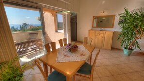 A dining area with a table, chairs, a potted plant, and a view of the sea through a sliding door. - Apartment Villa Molina (Zupa dubrovacka)