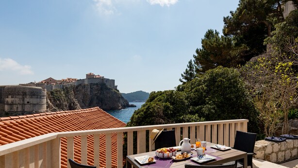 Ein Balkon mit Frühstückstisch, der Blick auf die Küste und eine historische Festung gewährt.