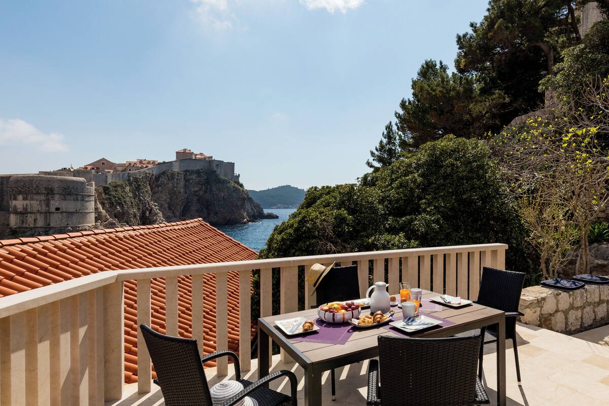 A balcony with a table set for breakfast overlooking a coastal view with a historic fort.