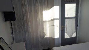 A bedroom with a bed, a door, a window, and a wall-mounted TV.