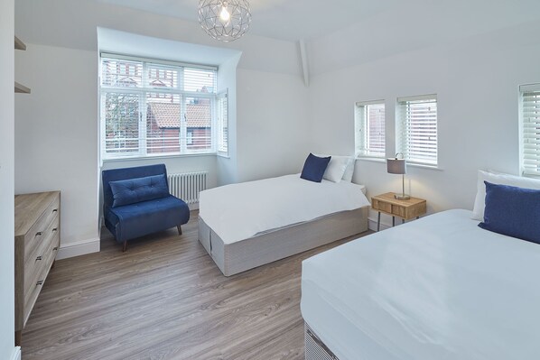 A bedroom with a bed, a chair, a bedside table, and a window.