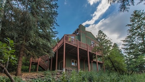 A rustic cabin with a wooden deck and a staircase leading to a second level.
