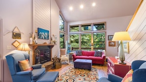 A cozy living room with a fireplace, a red sofa, blue armchairs, and a patterned rug.