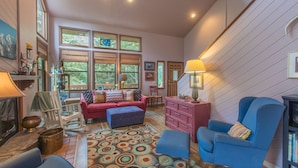 A spacious living room with a large window, a red sofa, a blue armchair, and a patterned rug.
