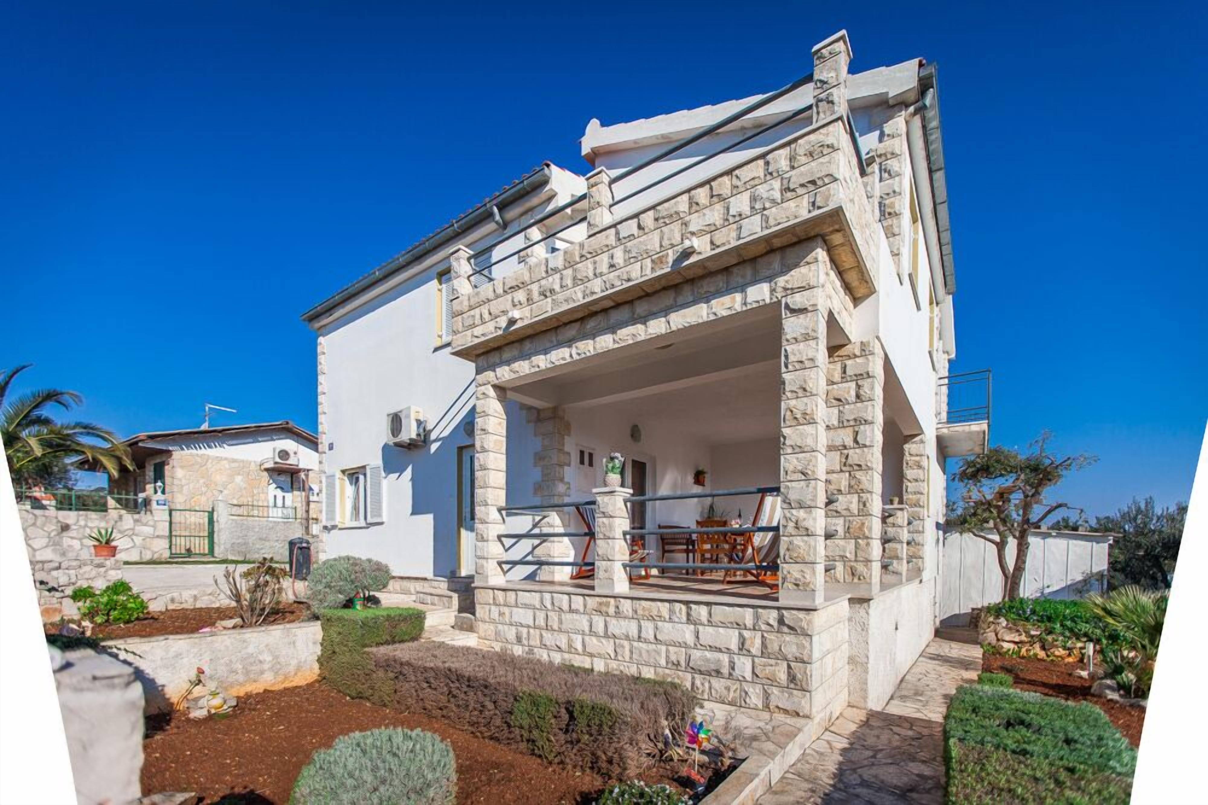 Une maison à deux étages avec une façade en pierre, un patio couvert agrémenté de meubles d’extérieur et un jardin bien entretenu.