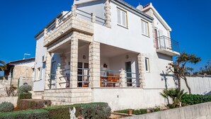 A two-story building with a balcony, stone columns, and a garden with a statue. - Apartments Irene's Place (Solta)