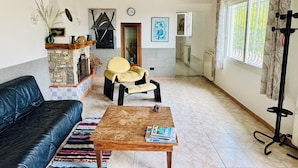 Una sala de estar acogedora con un sofá de cuero negro, una mesa de centro de madera con revistas, un sillón amarillo y una chimenea de piedra.
