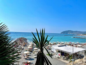A beach with umbrellas and sun loungers, a rocky shoreline, and a view of the sea and distant hills. - Casa Belvedere (Diano San Pietro)