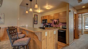 A kitchen with wooden cabinets, a bar area with stools, and pendant lighting. - Spacious 3-Bedroom + Loft Condo at Timber Run – Perfect for Families and Groups! (Steamboat Springs)
