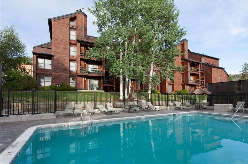 En modern byggnad med en swimmingpool, omgiven av träd och ett inhägnat område med solstolar.