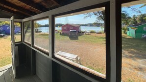 A room with a view of a lake, a red building, and a green building. - Lakefront  Yellow Cottage (Northwood)
