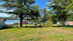 A campsite with small cabins, a grassy area, and a lake in the background. - Lakefront  Yellow Cottage (Northwood)