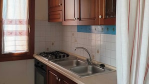 A kitchen with wooden cabinets, a gas stove, a sink, and a window with curtains. - A stone's throw from the center (San Teodoro)