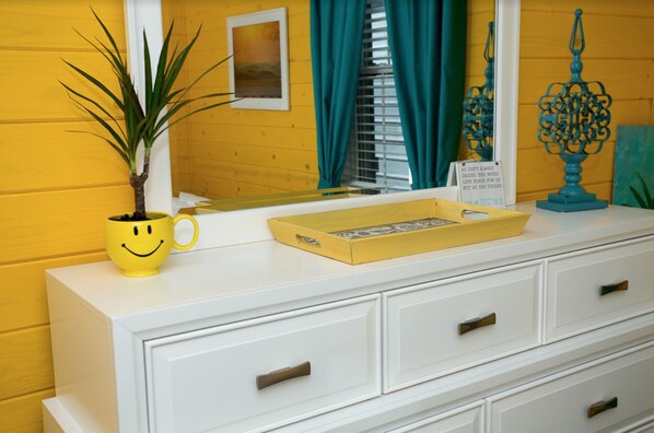 Een witte dressoir met lades, een gele mok met een smiley, een potplant en een dienblad met een fotolijst.