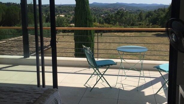 A bedroom with a large window overlooking a balcony with a table and chairs, a bed, and a view of the countryside. - Beautiful house with heated pool overlooking Barjac (Barjac)