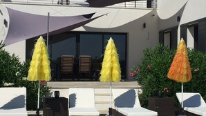 A poolside area with lounge chairs and umbrellas, a building with large windows, and a clear view of the pool. - Beautiful house with heated pool overlooking Barjac (Barjac)