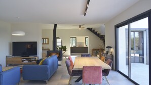 A modern living room with a large TV, blue sofas, a wooden dining table, and a staircase leading to an upper level. - Beautiful house with heated pool overlooking Barjac (Barjac)