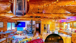 Ein gemütliches Blockhauskamin-Interieur mit Holzbalkendecke, einem Fernseher im Wohnbereich, einem Esstisch und einer Küche mit Holzschränken.