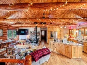 A wooden cabin interior with a dining area, kitchen, and a stone fireplace. - Rustic Charm: Pewaukee Lake Cabin, Sauna & Hot Tub (Pewaukee)
