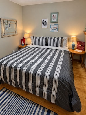 A neatly made bed with striped bedding, a bedside table with a lamp, and framed artwork on the wall. - Rustic Charm: Pewaukee Lake Cabin, Sauna & Hot Tub (Pewaukee)