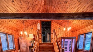 Ein Holzinnenraum mit einer zentralen Treppe, Holzwänden und einem Durchblick durch eine Tür nach draußen.