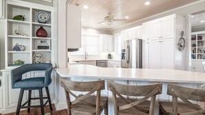 A spacious kitchen with white cabinetry, a large island with bar stools, and a ceiling fan.