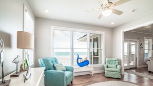 A spacious living room with a large window, a ceiling fan, and a view of the beach.
