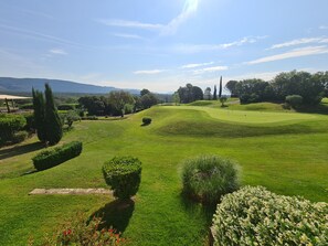 A golf course with well-maintained grass, trees, and rolling hills in the background.